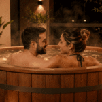 Ofurô redondo de madeira em área externa, com casal relaxando em água quente, cercado por plantas e iluminação aconchegante.